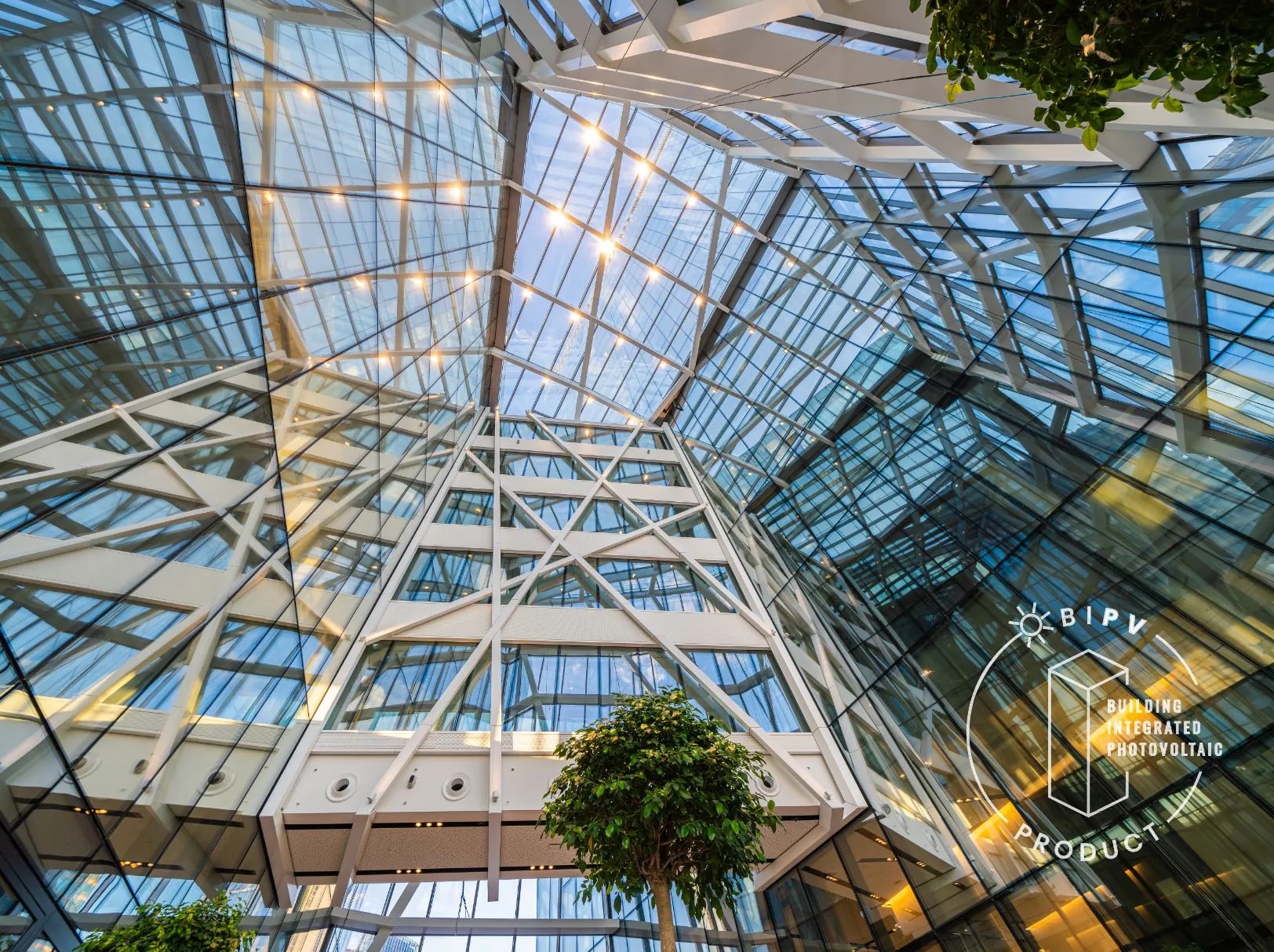 Interior view of a modern glass atrium with a geometric steel structure and large transparent facades, featuring integrated photovoltaic glass panels and natural greenery.